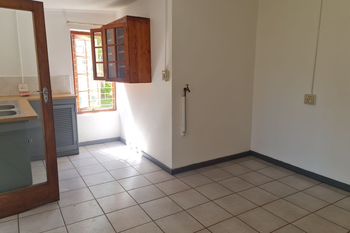 An empty kitchen area featuring tiled flooring, built-in cabinetry, and a wall-mounted tap, offering a blank canvas for renovation.