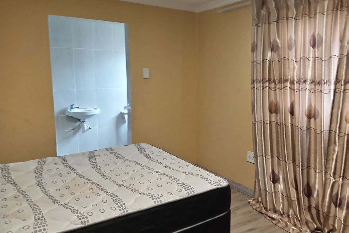 A bedroom featuring laminate flooring and an open-plan alcove containing a wall-mounted basin, requiring cosmetic updates to improve the overall aesthetic.