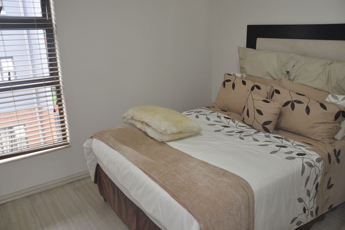 A functional bedroom featuring laminate flooring, neutral wall finishes, and venetian blinds providing natural light.