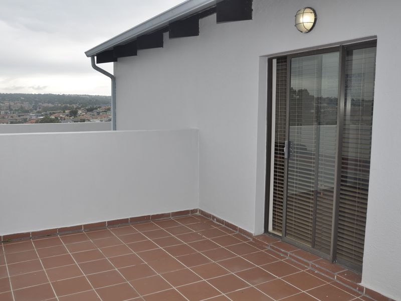 A clean, open-air balcony featuring terracotta tiled flooring, a sliding glass door entrance, and a parapet wall with views of the surrounding area.