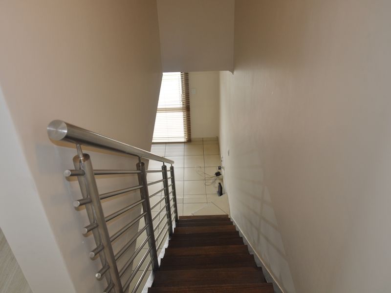 A view looking down a wooden staircase featuring a modern stainless steel balustrade, leading to a tiled landing area with natural light.