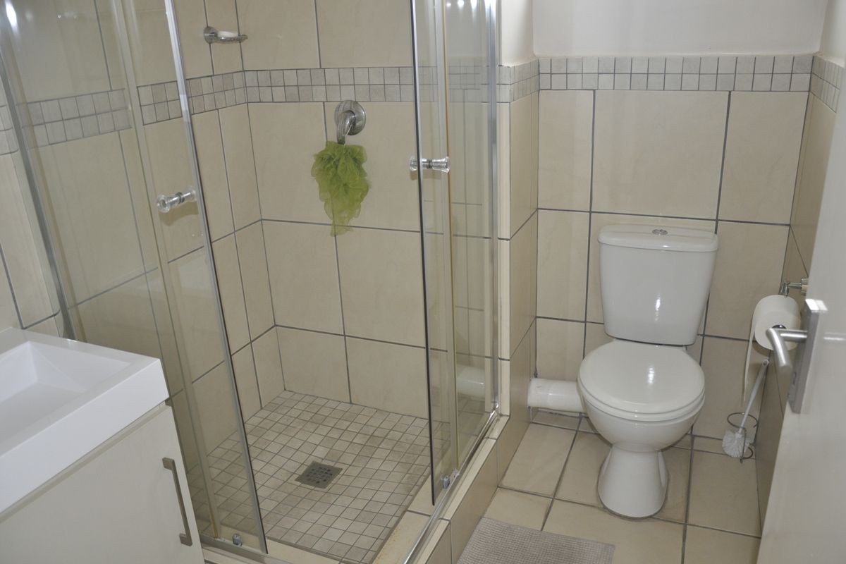 Compact bathroom featuring a glass shower enclosure, white toilet, and vanity basin with neutral wall and floor tiling.