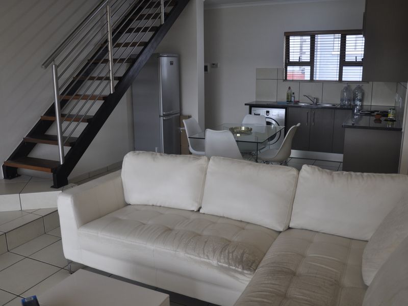 Open-plan living and kitchen area featuring tiled flooring, a modern staircase with metal balustrades, and functional kitchen cabinetry with a tiled backsplash.