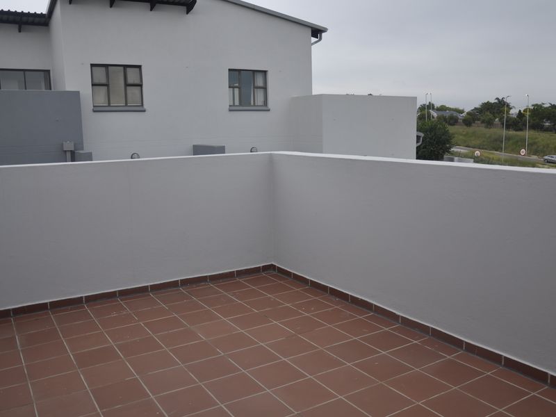 A spacious open-air balcony featuring terracotta-style floor tiles and a solid parapet wall, offering a clean and functional outdoor living space.