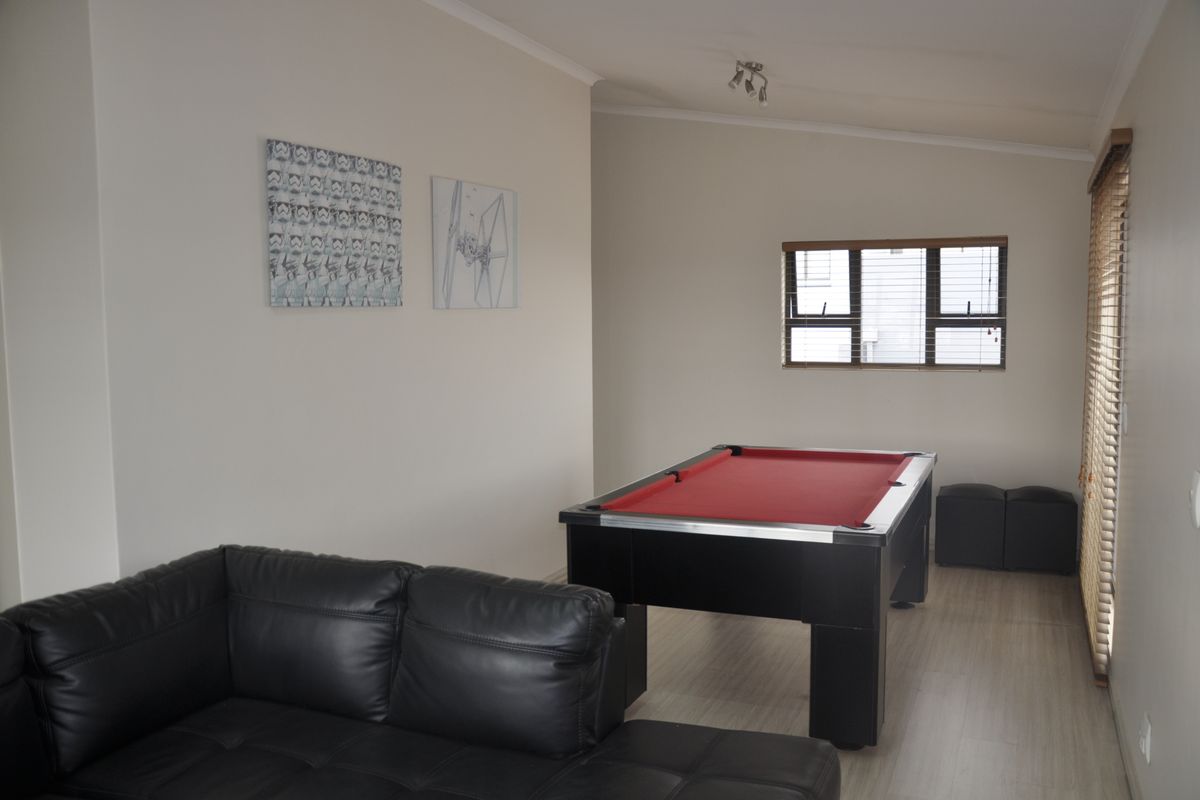 A spacious living area featuring light-toned laminate flooring, neutral wall finishes, and window blinds, currently utilized as a recreational space.