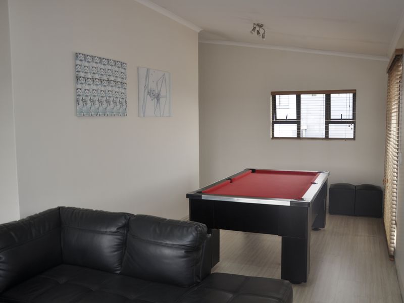 A spacious living area featuring light-toned laminate flooring, neutral wall finishes, and window blinds, currently utilized as a recreational space.