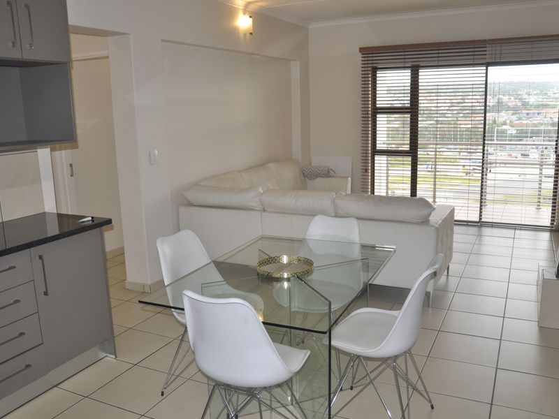 Open-plan living and dining area featuring tiled floors, modern grey kitchen cabinetry with granite countertops, and a large sliding door leading to a balcony.