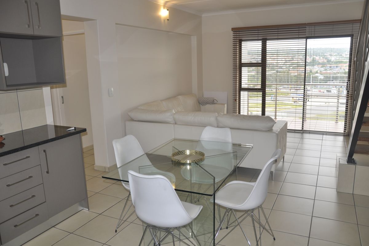 Open-plan living and dining area featuring tiled floors, modern grey kitchen cabinetry with granite countertops, and a large sliding door leading to a balcony.
