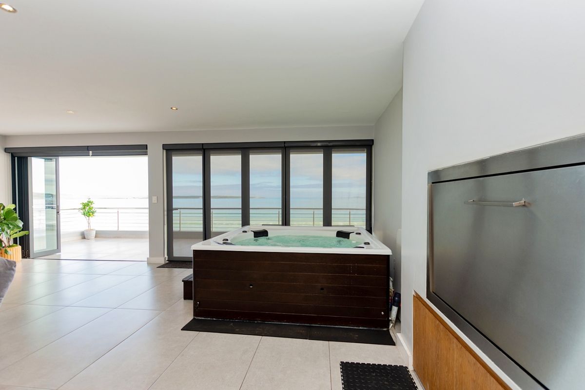 Spacious living area featuring a built-in jacuzzi, modern tiled flooring, and large bi-fold doors opening onto a balcony with scenic ocean views.