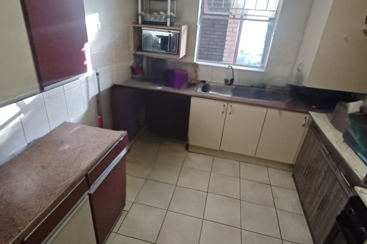 A functional kitchen featuring built-in cabinetry, a stainless steel sink, and tiled flooring, offering a practical layout with potential for modernization.