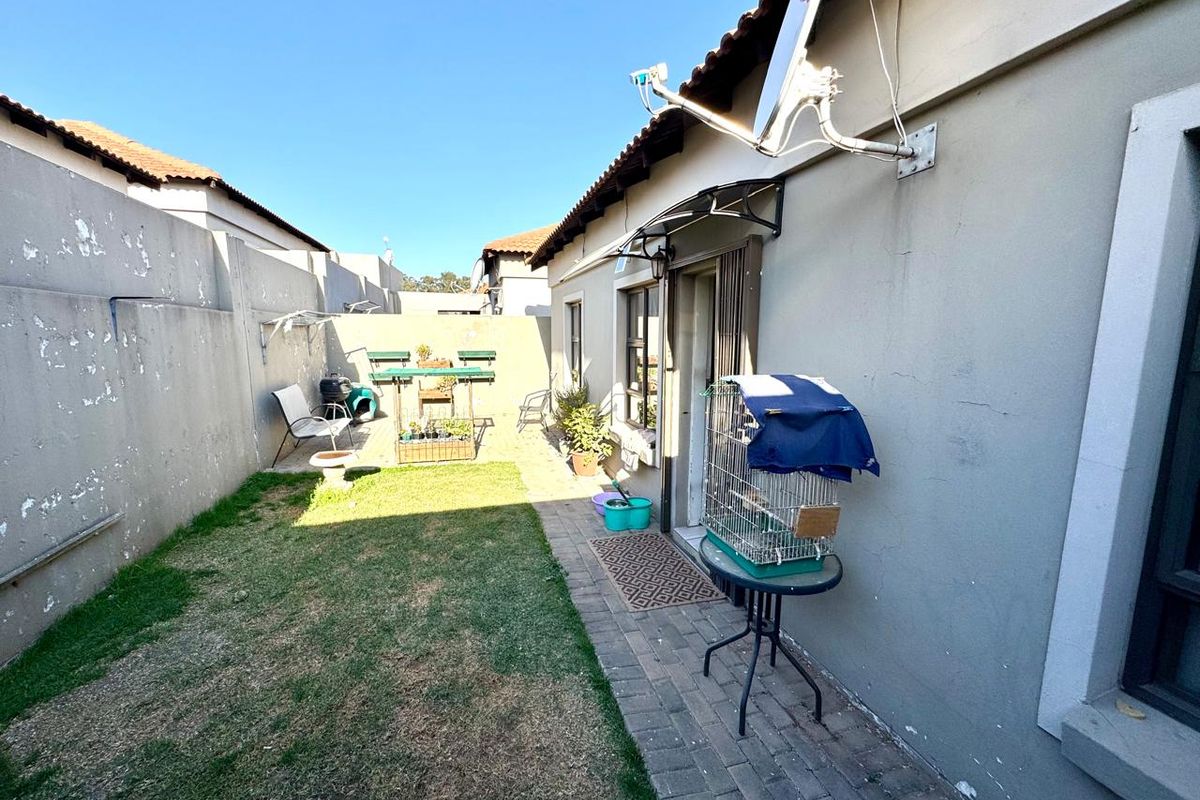 A private rear courtyard featuring a paved walkway, small lawn area, and high boundary walls, providing a compact outdoor space for the townhouse.