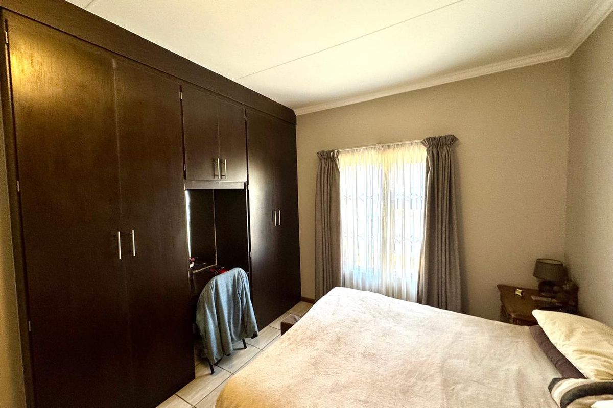 A bedroom featuring dark wood built-in cupboards with an integrated vanity area and tiled flooring.