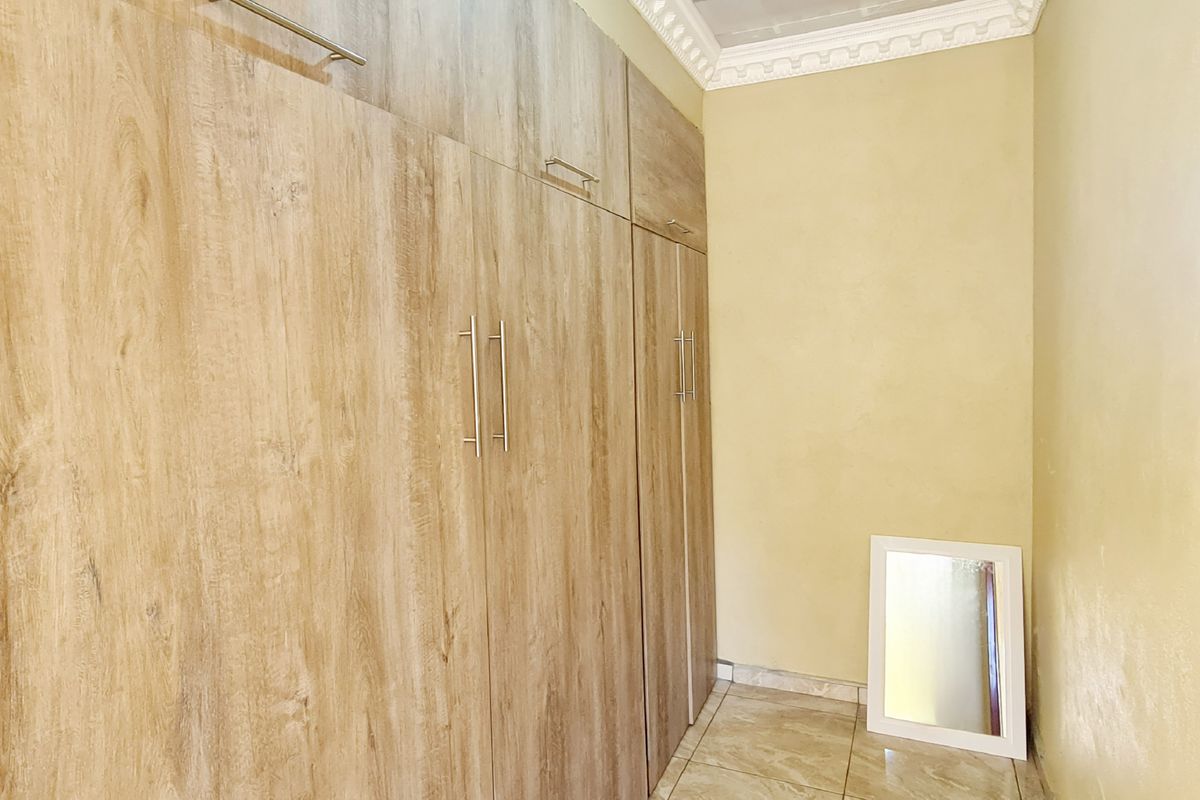 A bedroom featuring built-in wooden cupboards with modern handles, tiled flooring, and decorative ceiling cornicing.