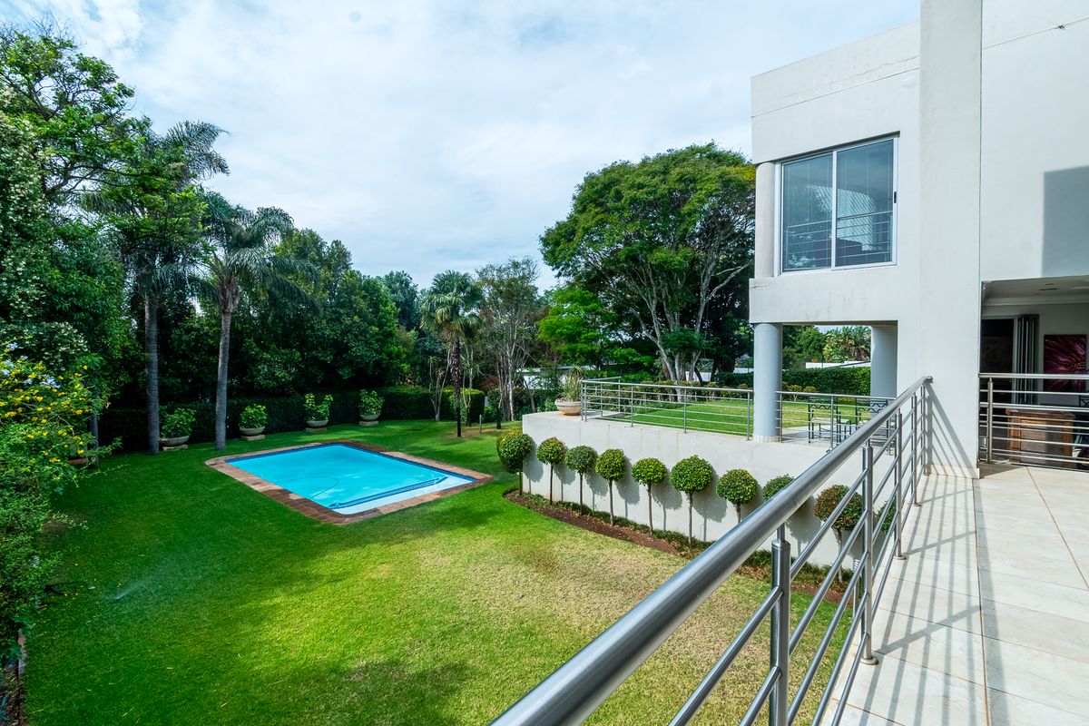 A spacious rear exterior view featuring a well-maintained garden, a swimming pool, and a tiled patio area with modern stainless steel balustrades.