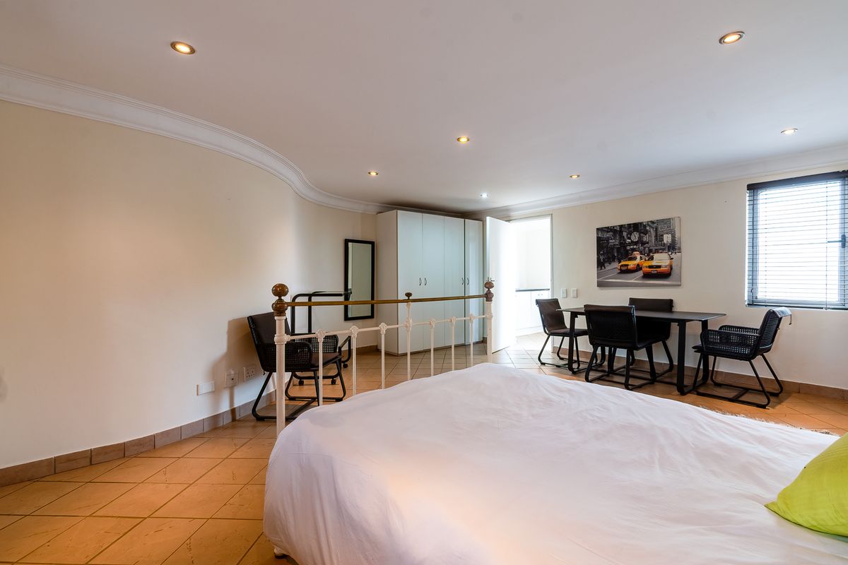 A spacious bedroom featuring tiled flooring, built-in cupboards, and recessed downlighting, offering a functional layout with natural light from the window.