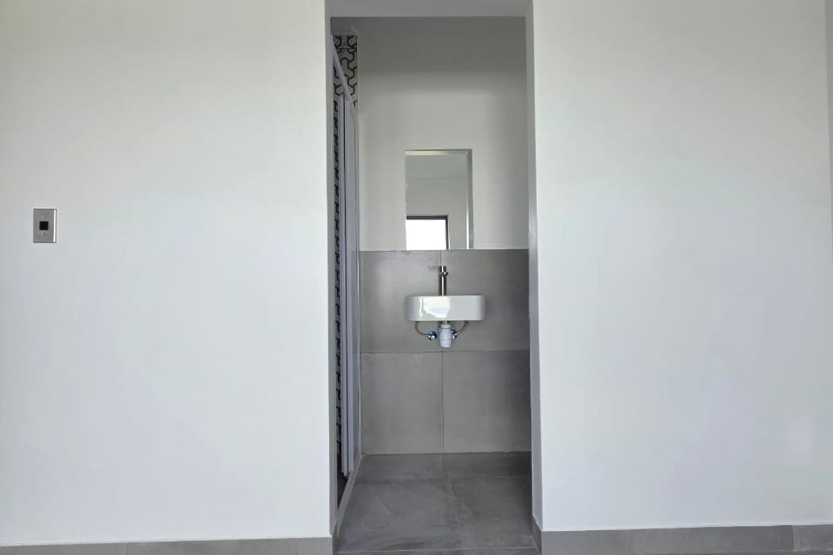 A clean, modern bathroom featuring large-format grey floor tiles, a wall-mounted basin, and a minimalist aesthetic.