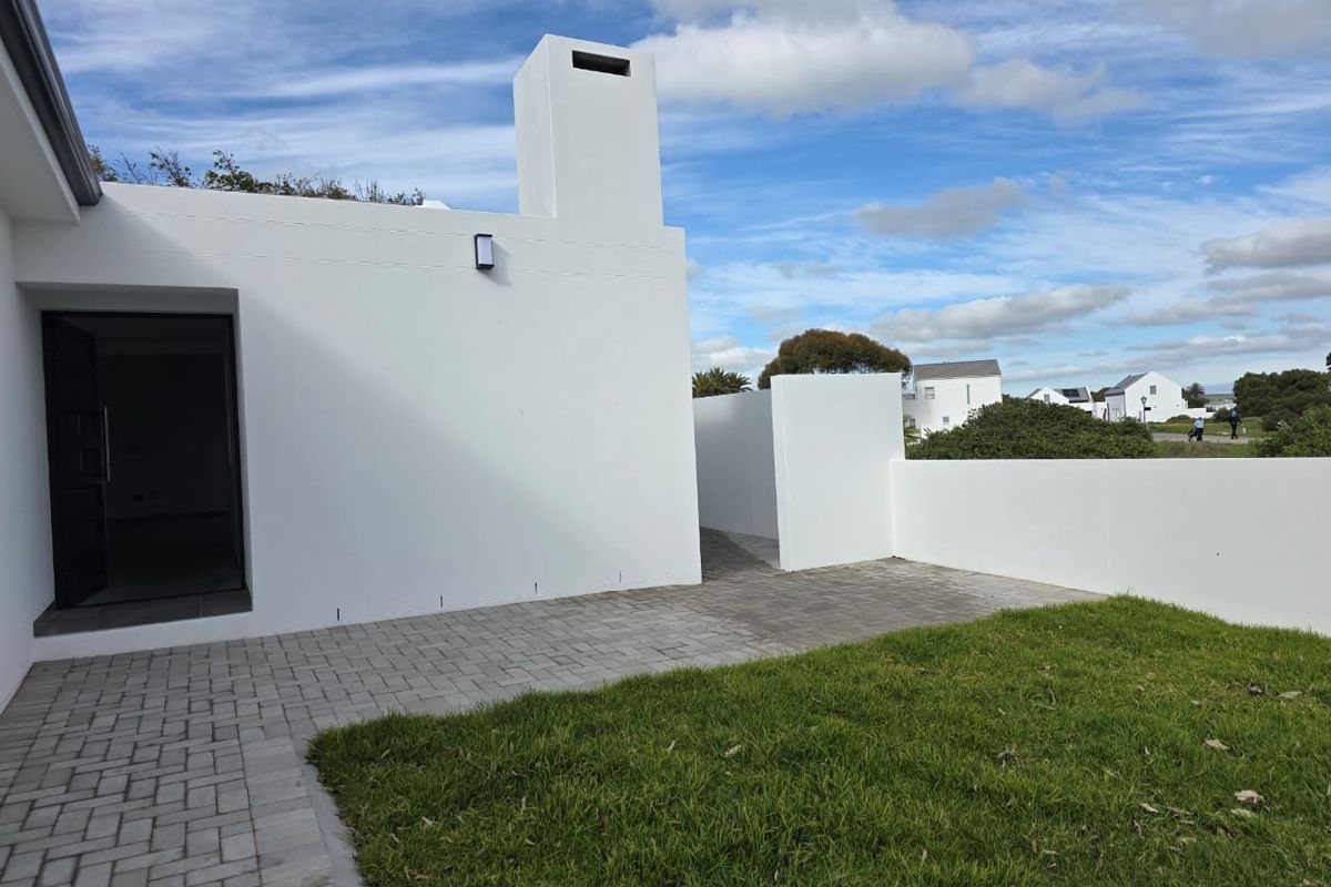 A modern exterior rear view featuring a paved patio area, a white rendered chimney stack, and a well-maintained lawn.