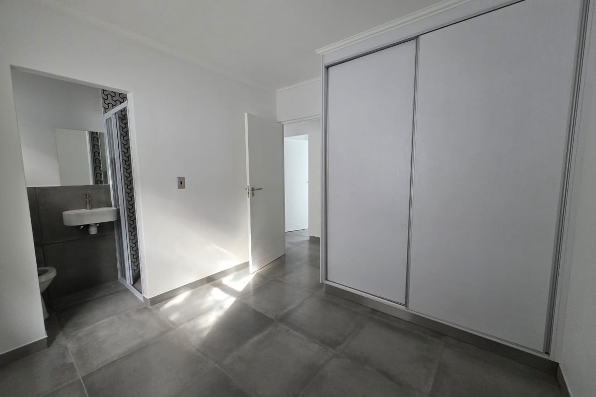 A modern bedroom featuring large format grey floor tiles, built-in sliding door cupboards, and an en-suite bathroom with contemporary finishes.