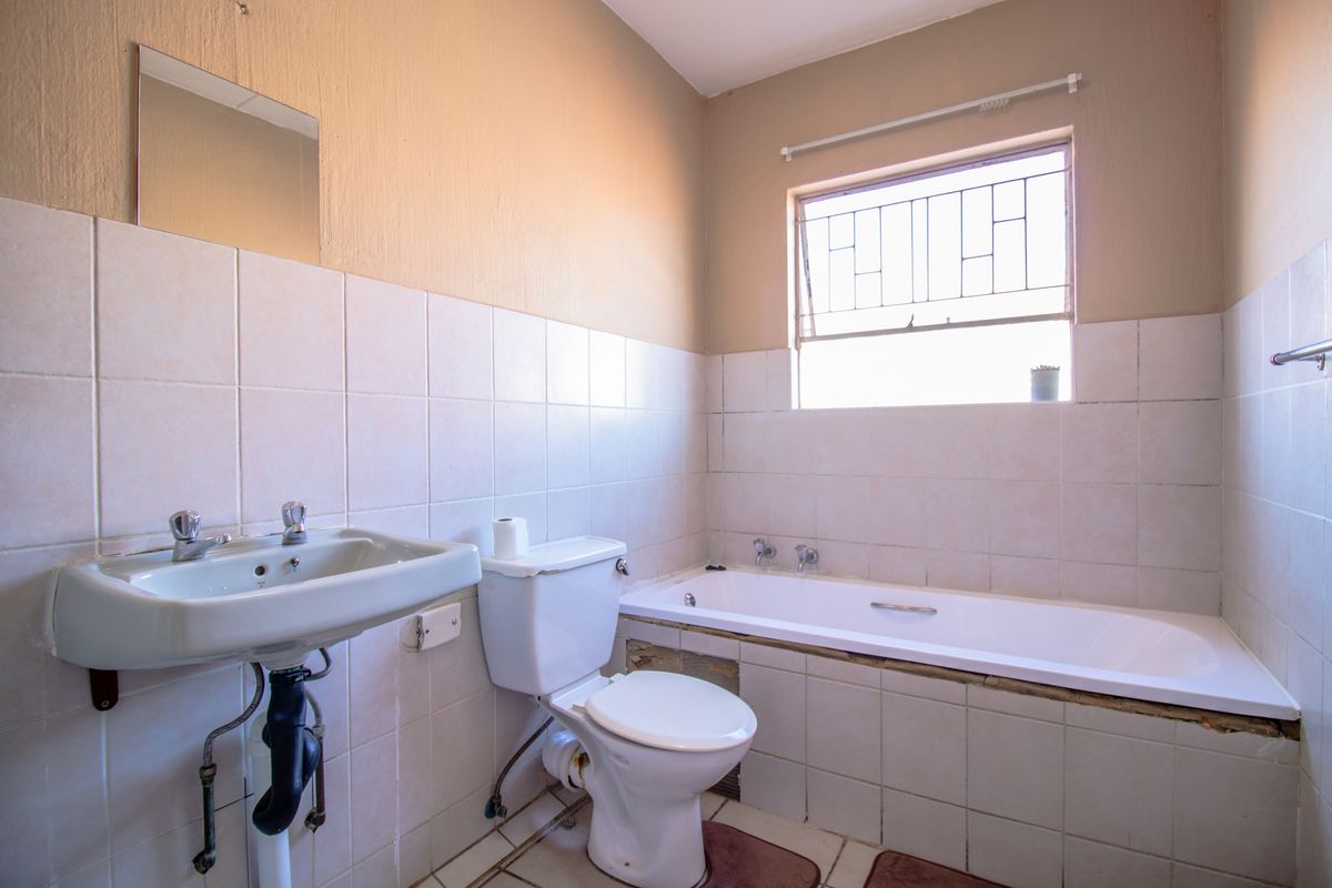 A functional bathroom featuring a wall-mounted basin, toilet, and built-in bathtub with tiled splashbacks and security bars on the window.