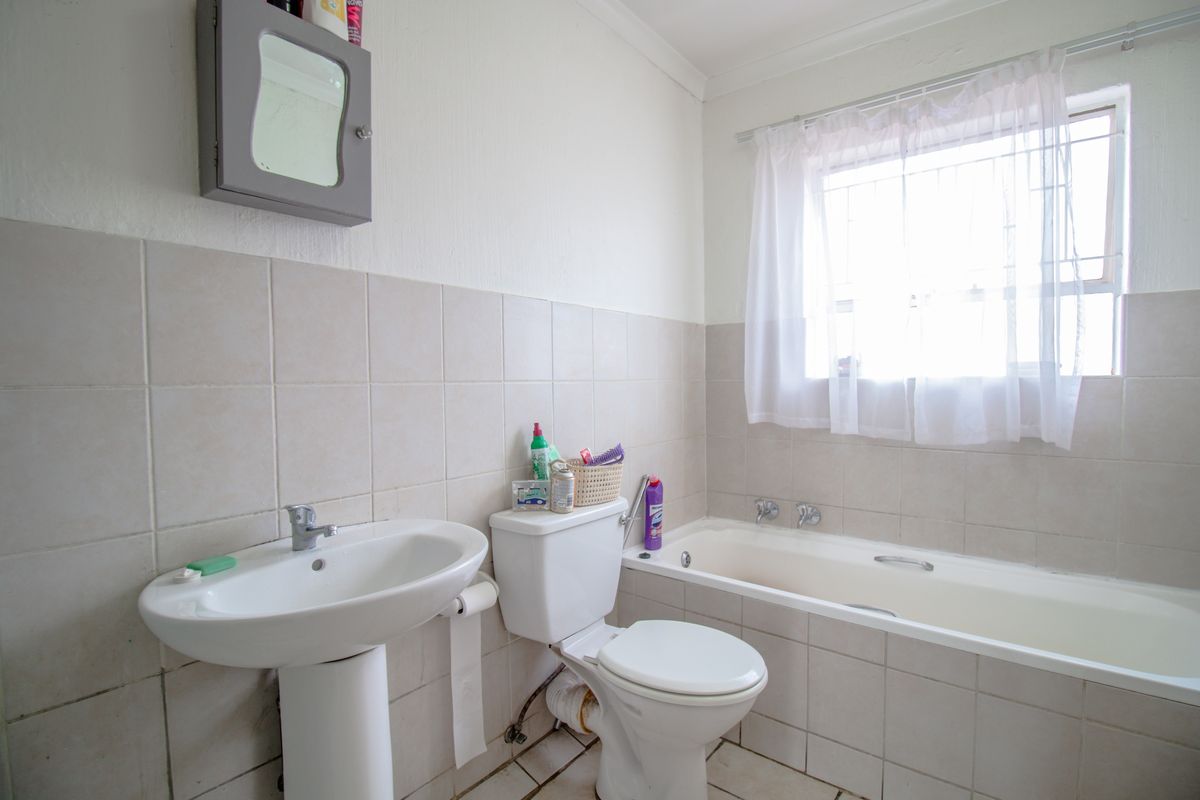 A functional bathroom featuring a pedestal basin, toilet, and built-in bathtub with neutral wall tiling and natural light from the window.