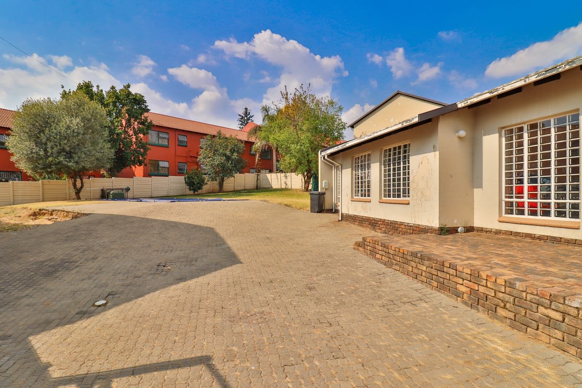 Rear exterior view of the property featuring a paved driveway, brick retaining wall, and security-fitted windows with visible exterior maintenance required.
