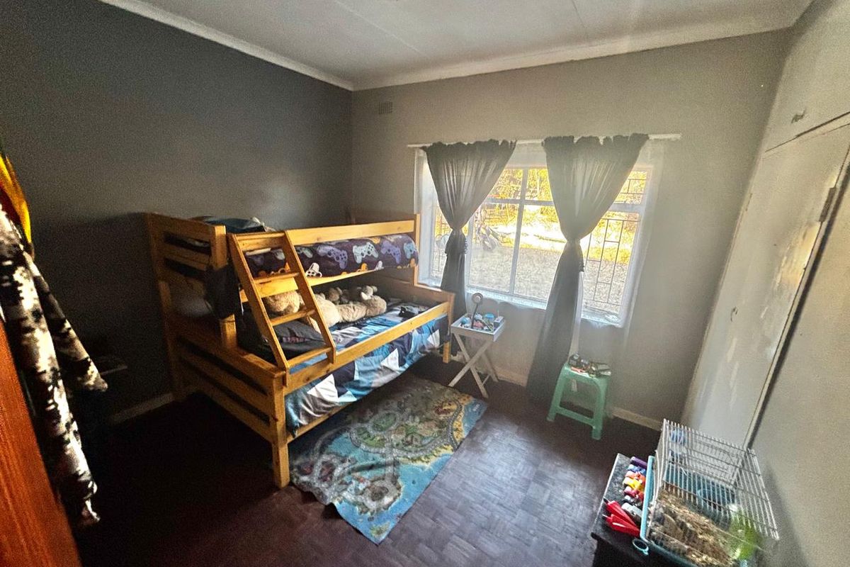 A bedroom featuring dark parquet flooring, built-in cupboards, and a window with security bars, providing natural light.