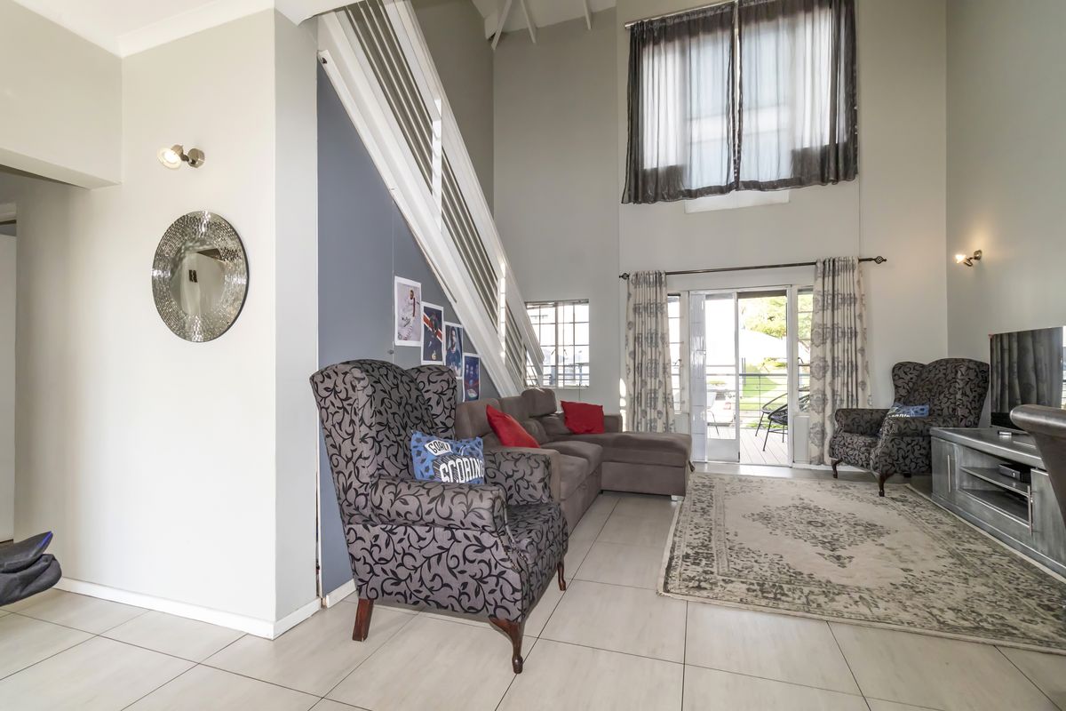 Spacious double-volume living area featuring tiled flooring, a staircase with a modern balustrade, and large glass sliding doors leading to an outdoor patio.