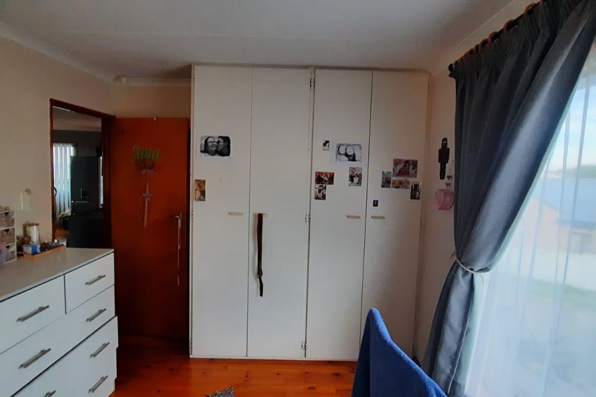 A bedroom featuring built-in cupboards and polished wooden flooring, with natural light entering through a large window.