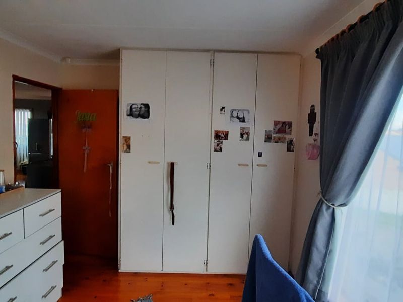 A bedroom featuring built-in cupboards and polished wooden flooring, with natural light entering through a large window.