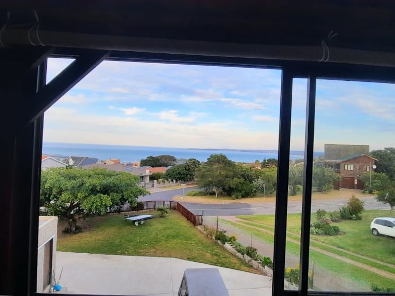 A scenic elevated view overlooking the surrounding neighborhood, garden, and distant ocean horizon, framed by a sliding glass door.