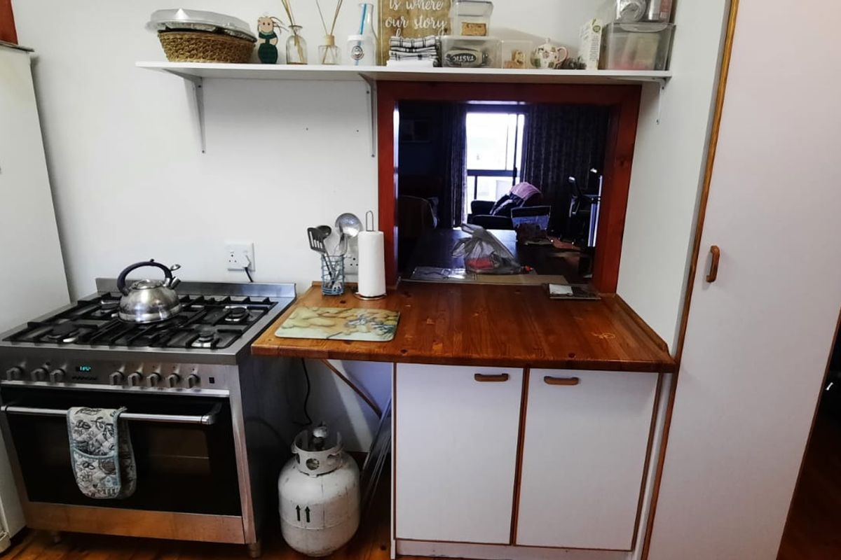A functional kitchen featuring a gas stove, wooden countertop, and a serving hatch opening into the living area.