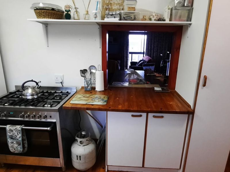 A functional kitchen featuring a gas stove, wooden countertop, and a serving hatch opening into the living area.