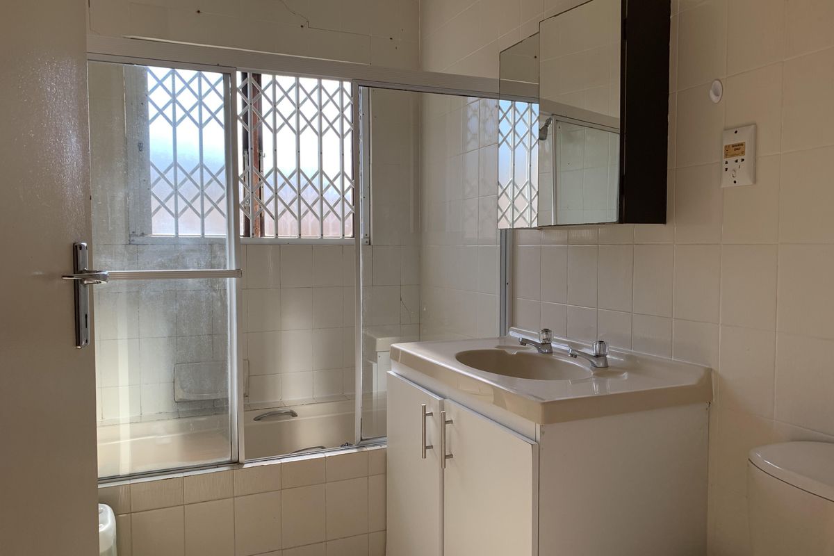 A dated bathroom featuring a vanity cabinet, bathtub with shower screen, and tiled walls. The space is ready for a modern renovation.