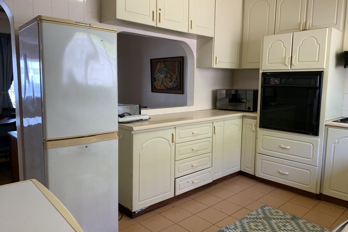 A dated kitchen featuring traditional cabinetry, built-in oven, and a convenient serving hatch opening into the adjacent living area.