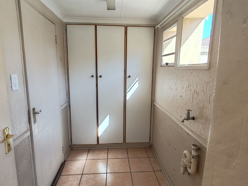 A functional laundry area featuring built-in storage cupboards, tiled flooring, and dedicated plumbing connections for a washing machine.