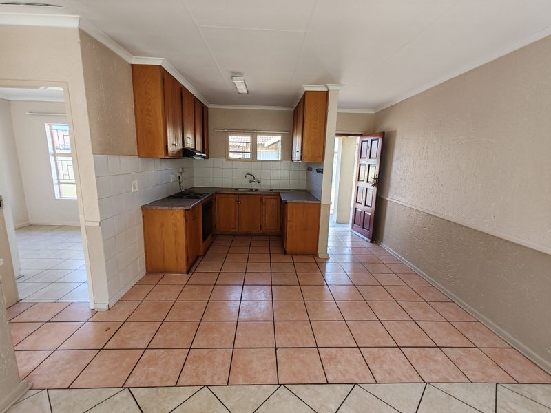 A functional kitchen featuring wooden cabinetry, tiled flooring, and a tiled backsplash, offering a clean, empty space ready for modernization.