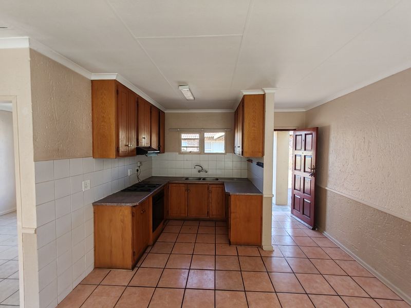 A functional kitchen featuring wooden cabinetry, built-in oven and hob, tiled splashbacks, and tiled flooring, offering a clean and practical layout.