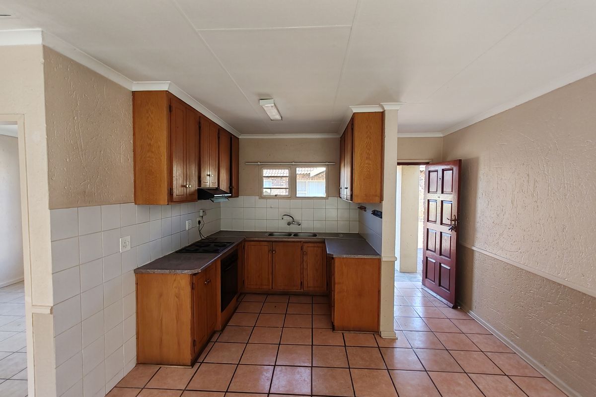 A functional kitchen featuring wooden cabinetry, built-in oven and hob, tiled splashbacks, and tiled flooring, offering a clean and practical layout.