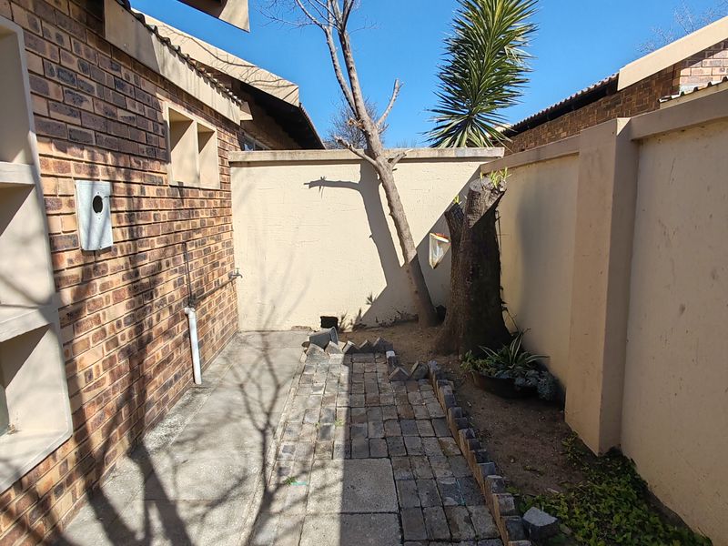 A narrow rear exterior courtyard featuring brick paving, boundary walls, and an external water tap, requiring maintenance and landscaping.