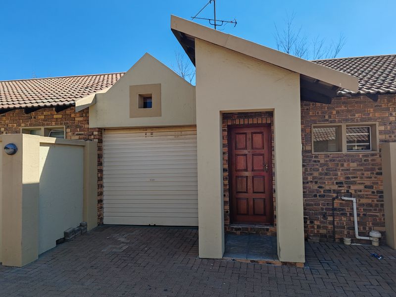Front elevation of the flat featuring a face brick facade, a roll-up garage door, and a timber entrance door with a paved driveway.