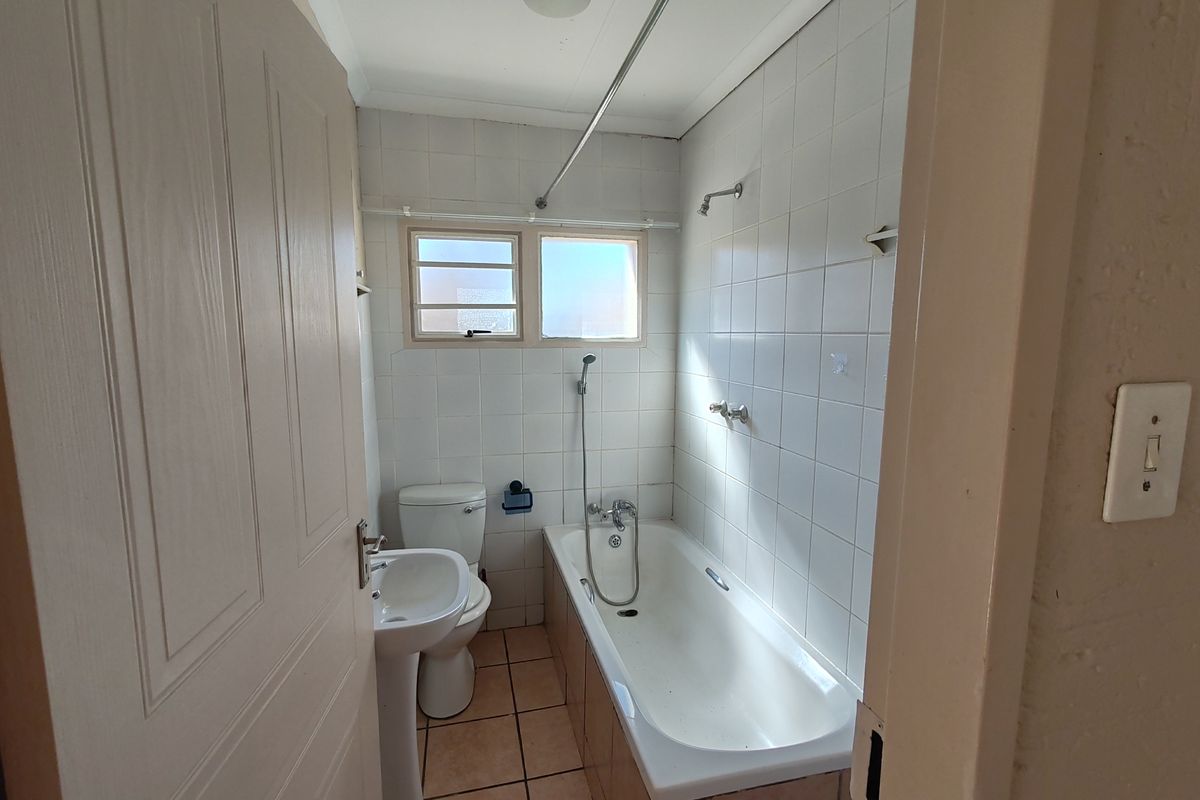 A functional bathroom featuring a pedestal basin, toilet, and a bathtub with shower mixer, finished with tiled walls and flooring.