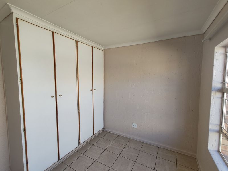 A vacant bedroom featuring built-in cupboards, tiled flooring, and security bars on the window.