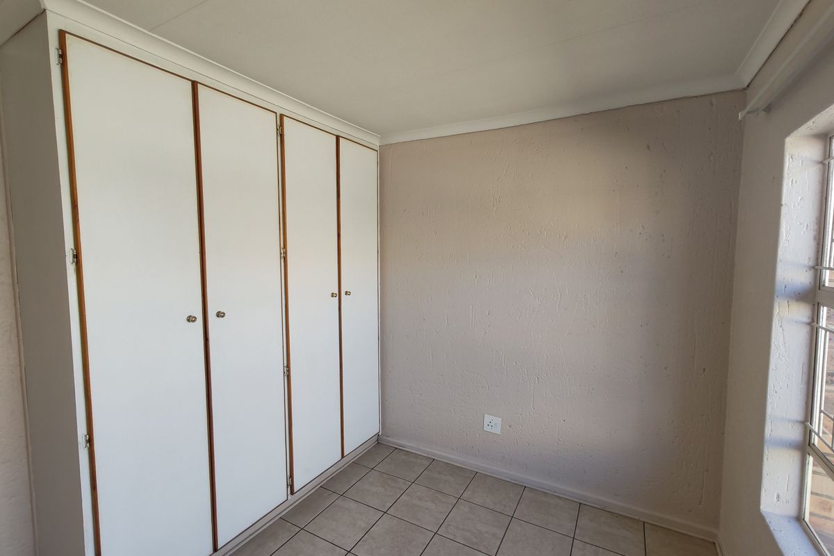 A vacant bedroom featuring built-in cupboards, tiled flooring, and security bars on the window.