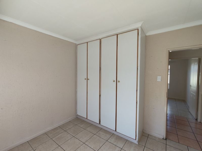 A bedroom featuring built-in cupboards, tiled flooring, and coved ceilings, presenting a clean, empty space ready for personalization.