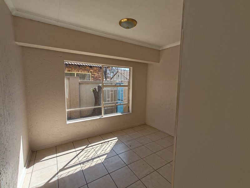 An empty bedroom featuring tiled flooring, a window with security bars, and a flush mount ceiling light, requiring minor cosmetic updates.