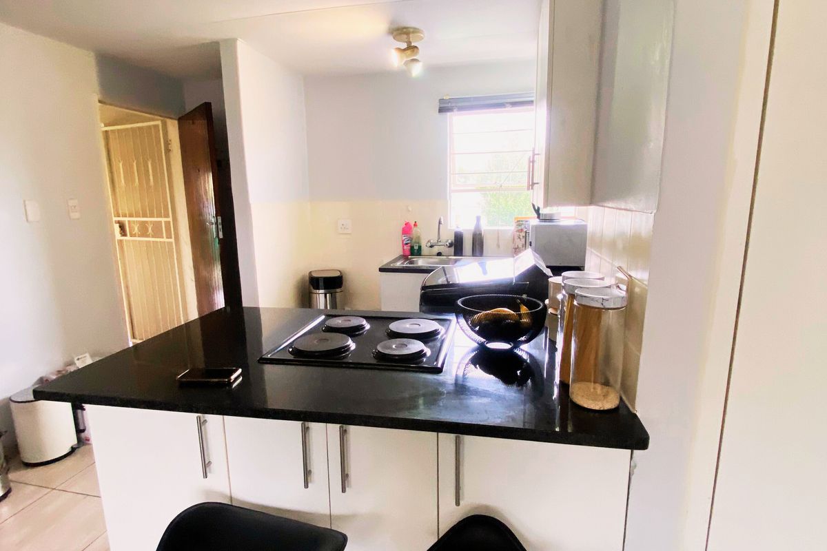 Compact kitchen featuring a black granite breakfast bar, built-in electric hob, and white cabinetry with tiled flooring.