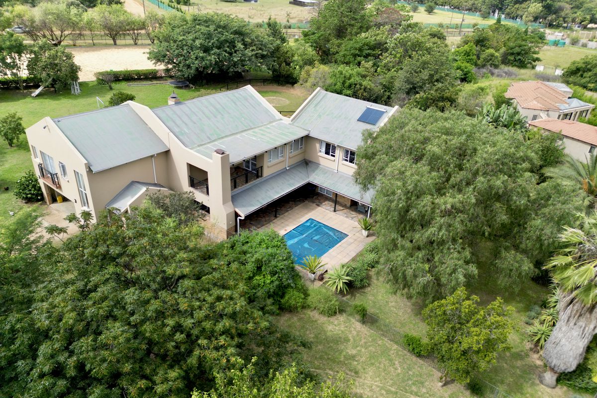 Aerial view of a large residential property featuring a multi-level house, a swimming pool, covered patio, and extensive landscaped garden surroundings.