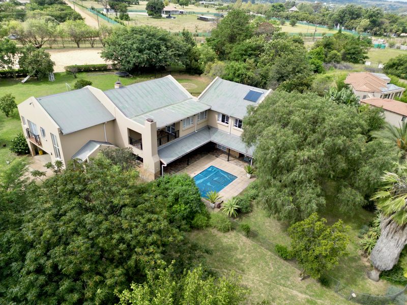 Aerial view of a large residential property featuring a multi-level house, a swimming pool, covered patio, and extensive landscaped garden surroundings.