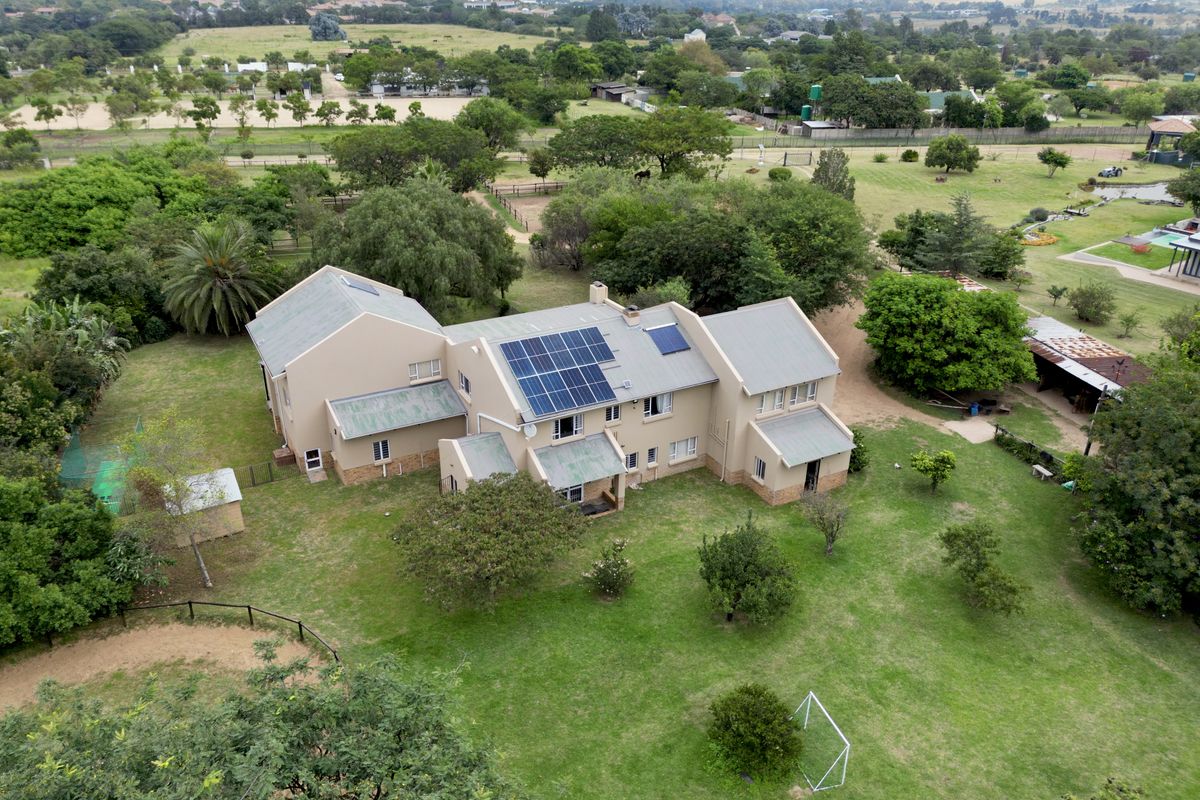 Aerial view of a large residential property featuring a multi-level house with solar panels, set within a spacious, well-maintained garden and rural landscape.