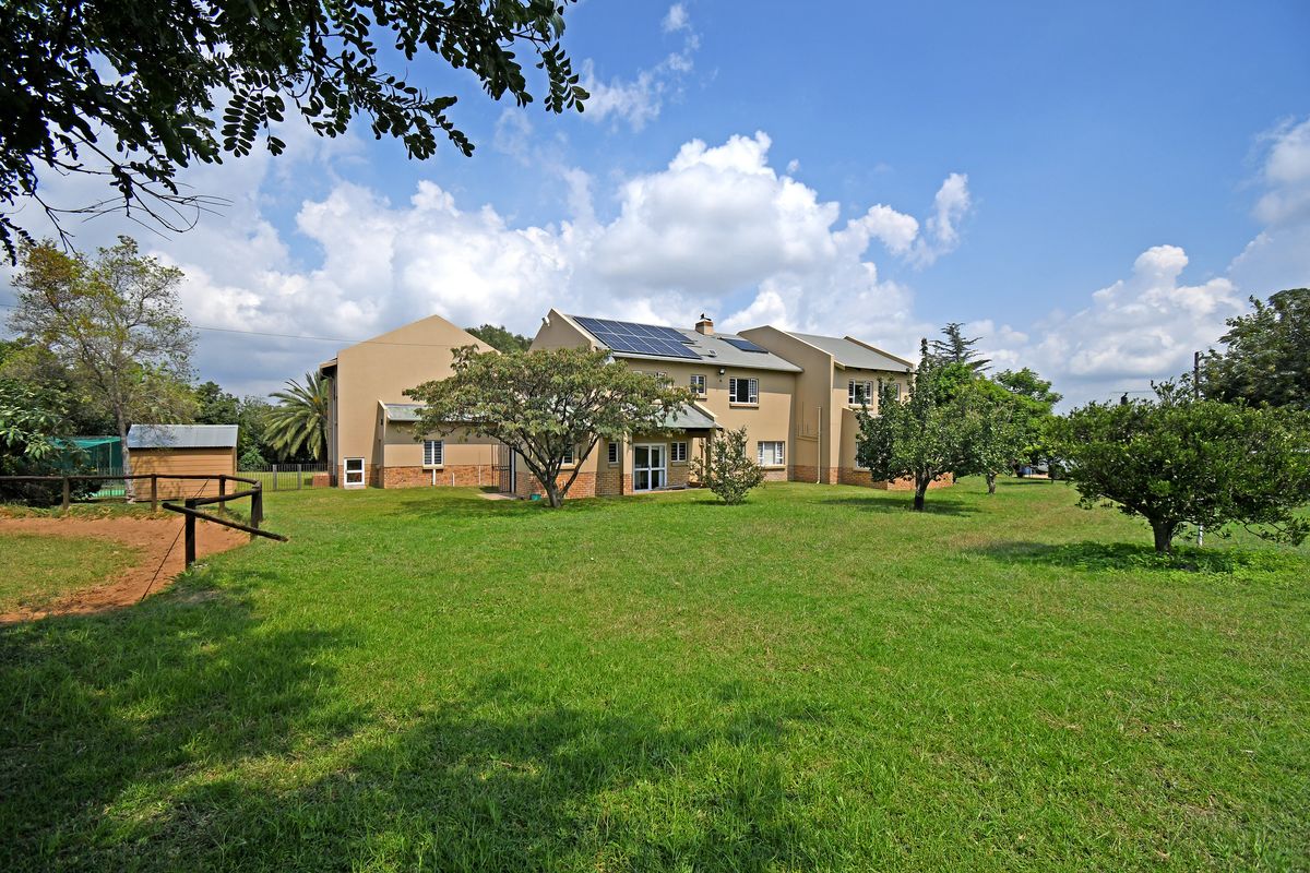 Rear view of the house featuring a large lawn, mature trees, and solar panels installed on the roof.